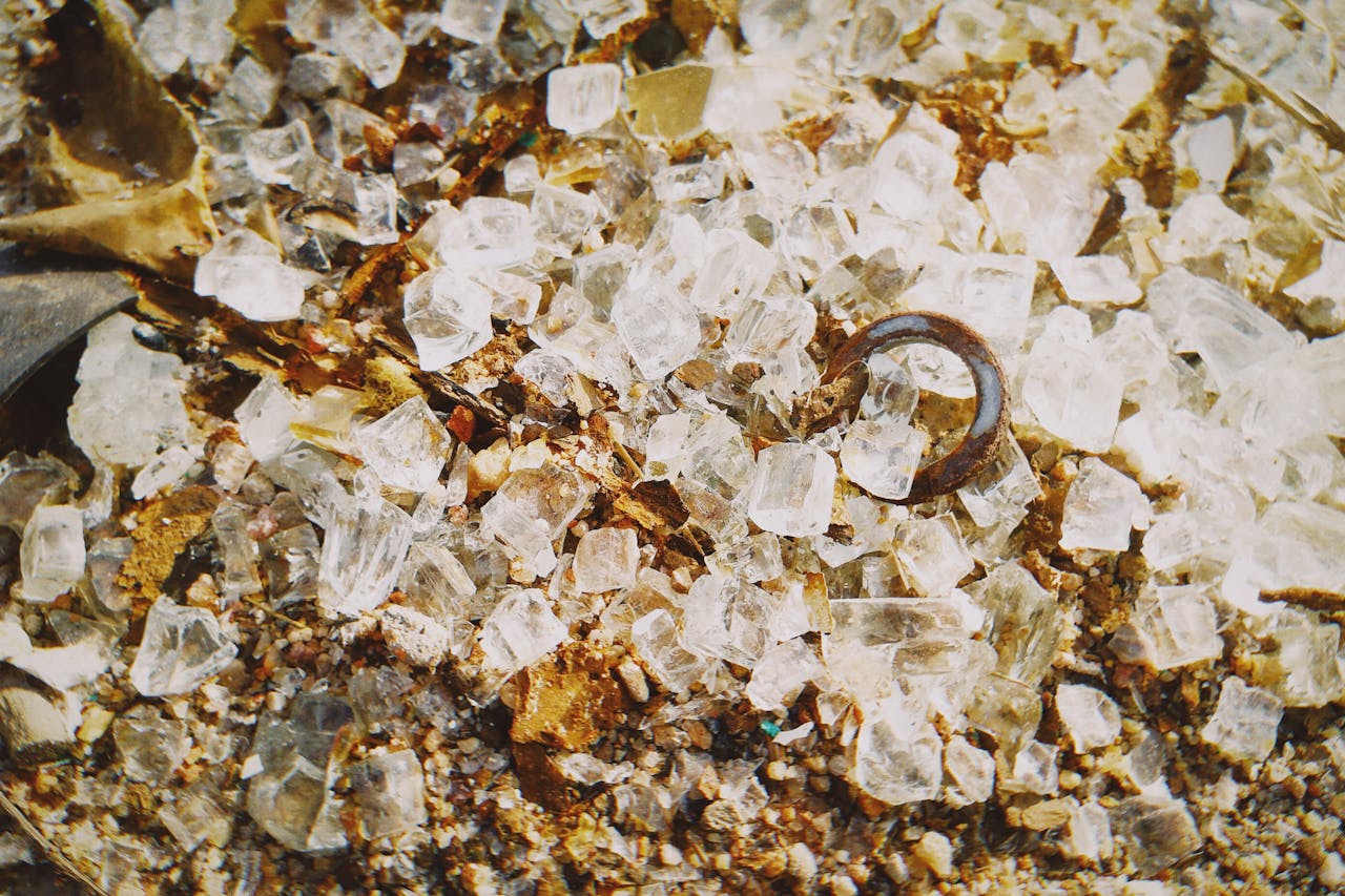 Detailed view of rough rock salt crystals scattered on a brown sandy surface with rusty metal object.