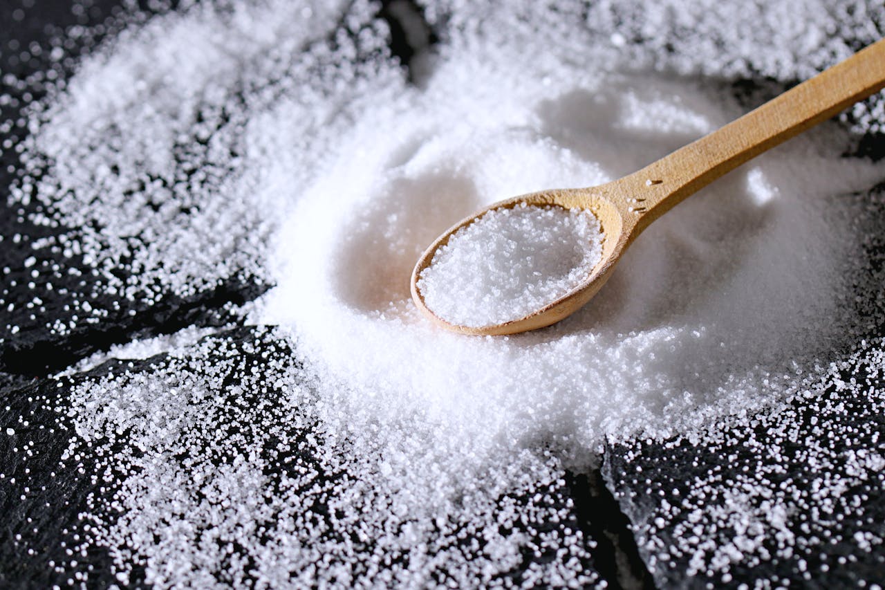 A close-up view of coarse sea salt on a dark surface with a wooden spoon.